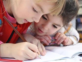 Two young girls draw in a notebook.